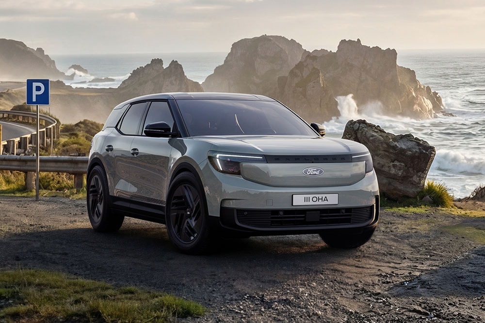 Silver Ford Explorer Collection parked on a road next to a rocky shoreline.