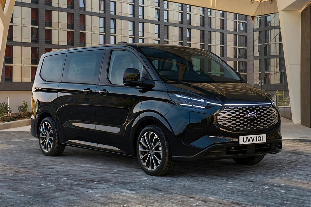 A black Ford E-Tourneo Custom is parked in front of a modern building.
