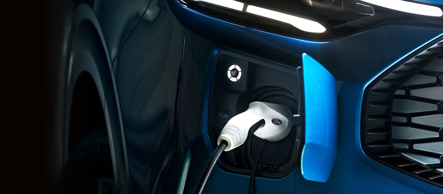 A close-up of the charging port of a blue Ford Tourneo Custom, with the charging cable plugged in.