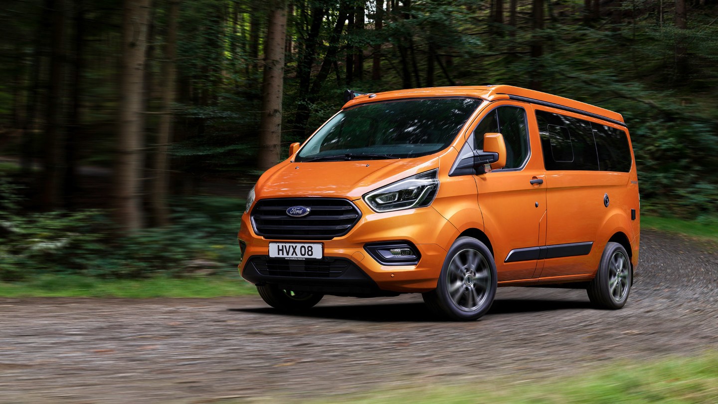 Orange Ford Transit Custom Nugget driving in forest Orange Ford Transit Custom Nugget driving in forest