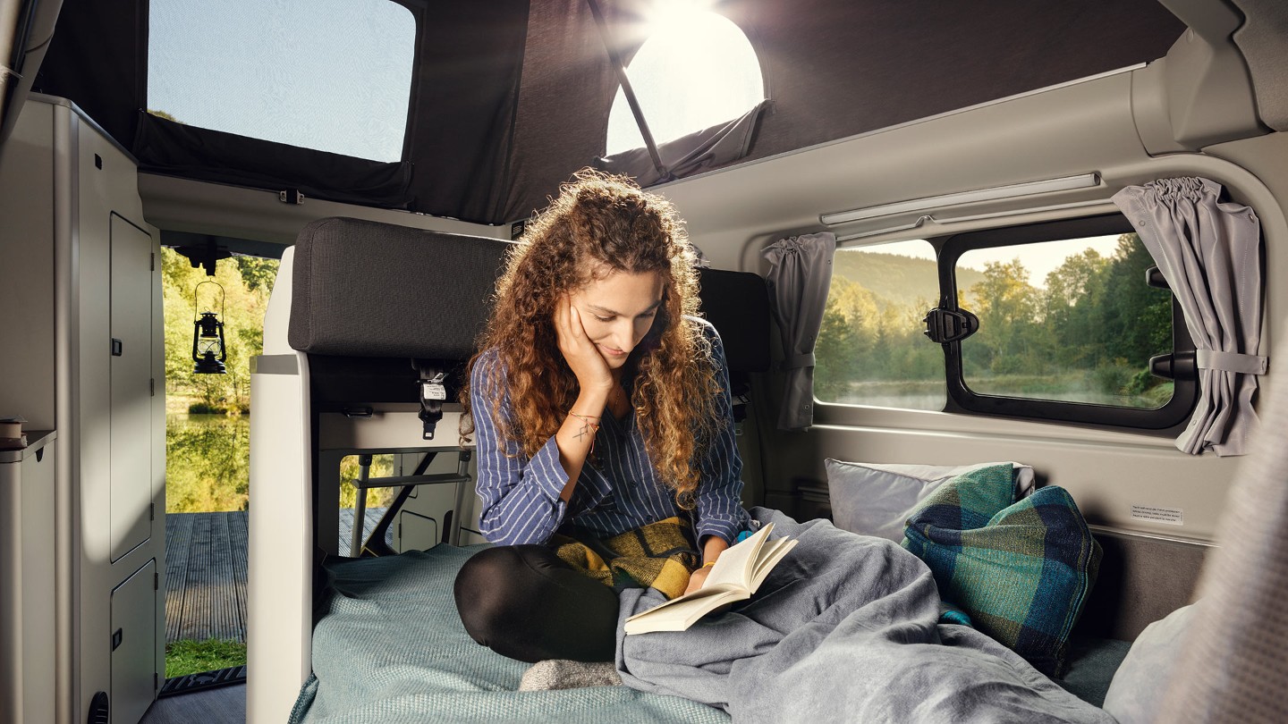 Woman siting and reading in Ford Transit Custom Nugget interior with lifted roof Woman siting and reading in Ford Transit Custom Nugget interior with lifted roof