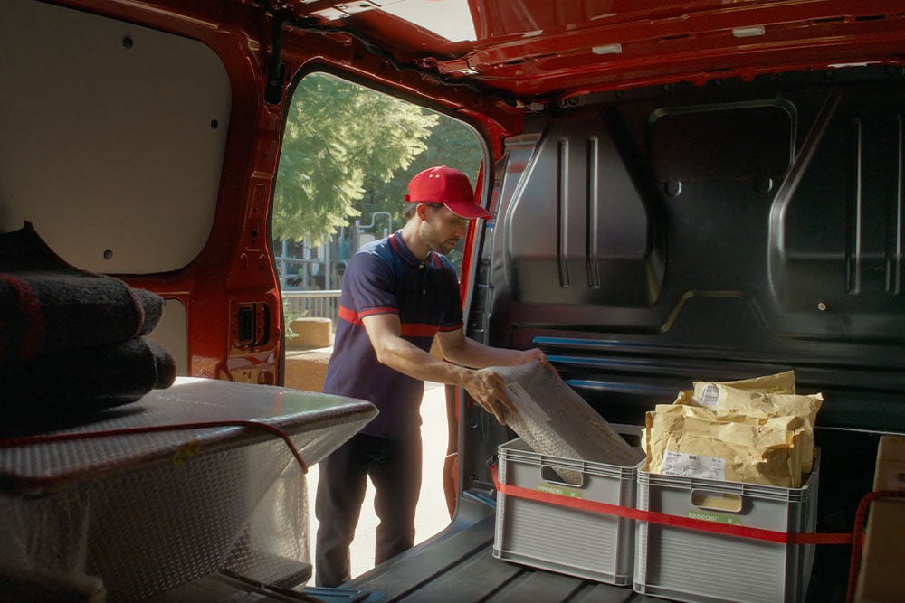 Delivery driver loading packages into a red Ford Transit Custom.