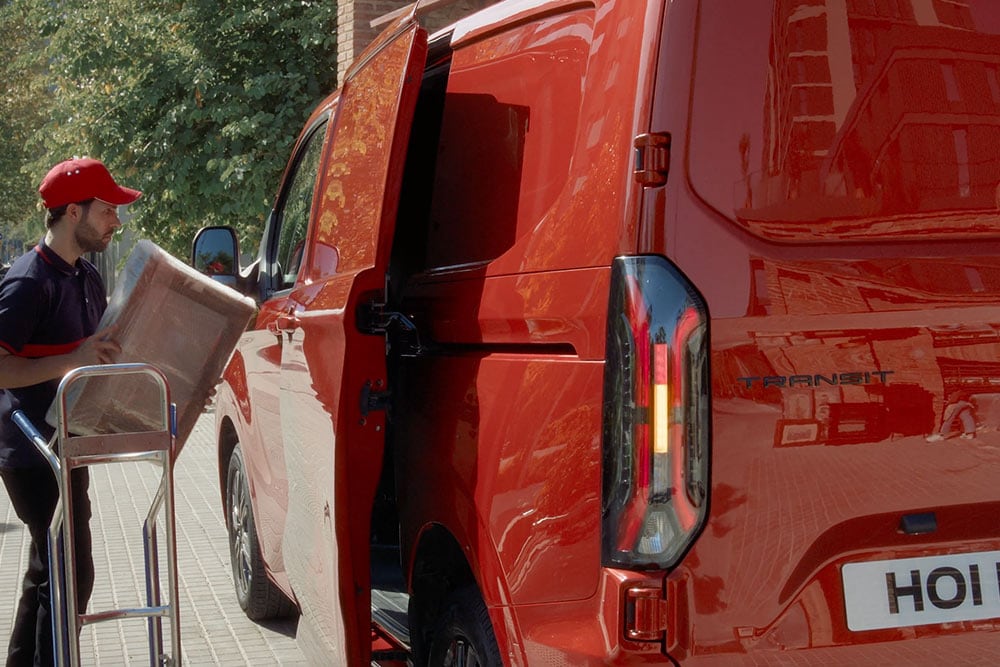 Delivery person unloading packages from a red Ford Transit Custom.