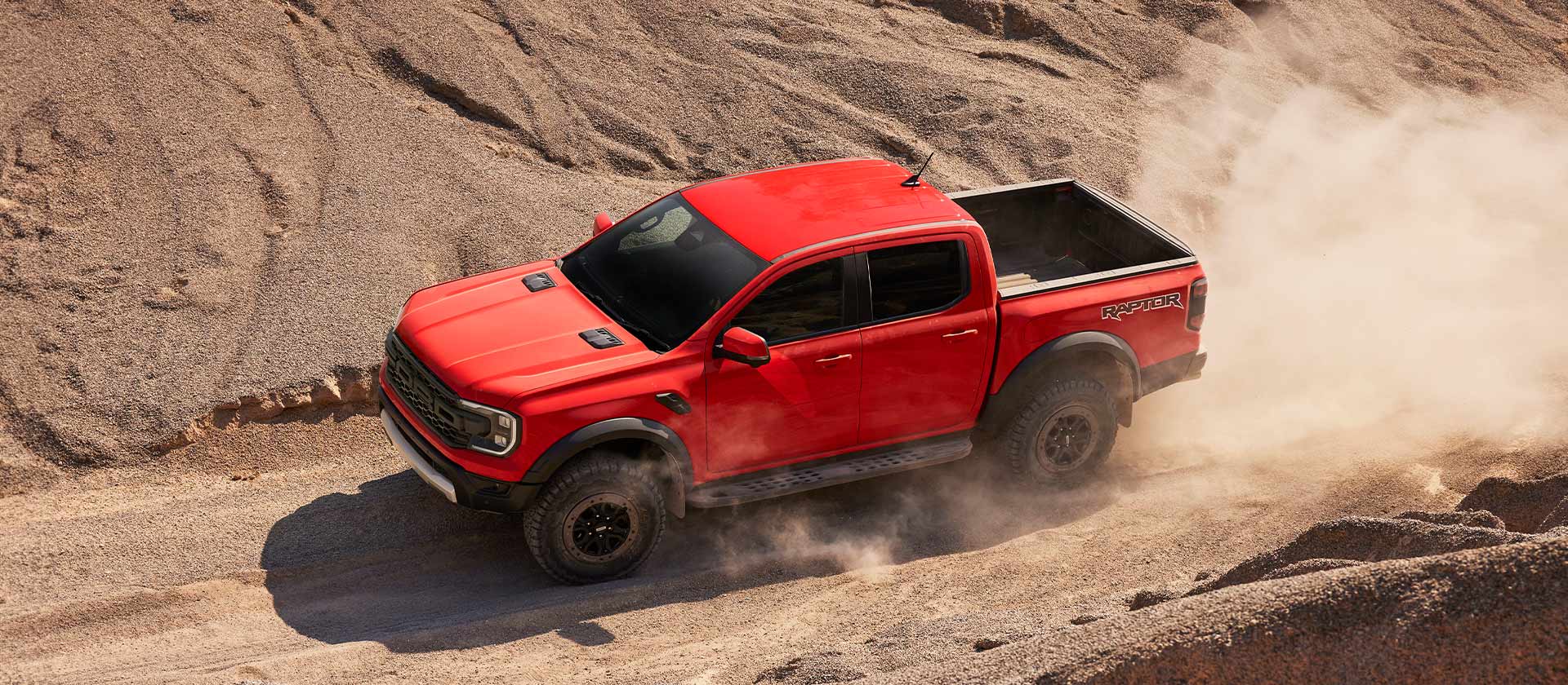 Code Orange Ford Ranger Raptor driving uphill through dust.
