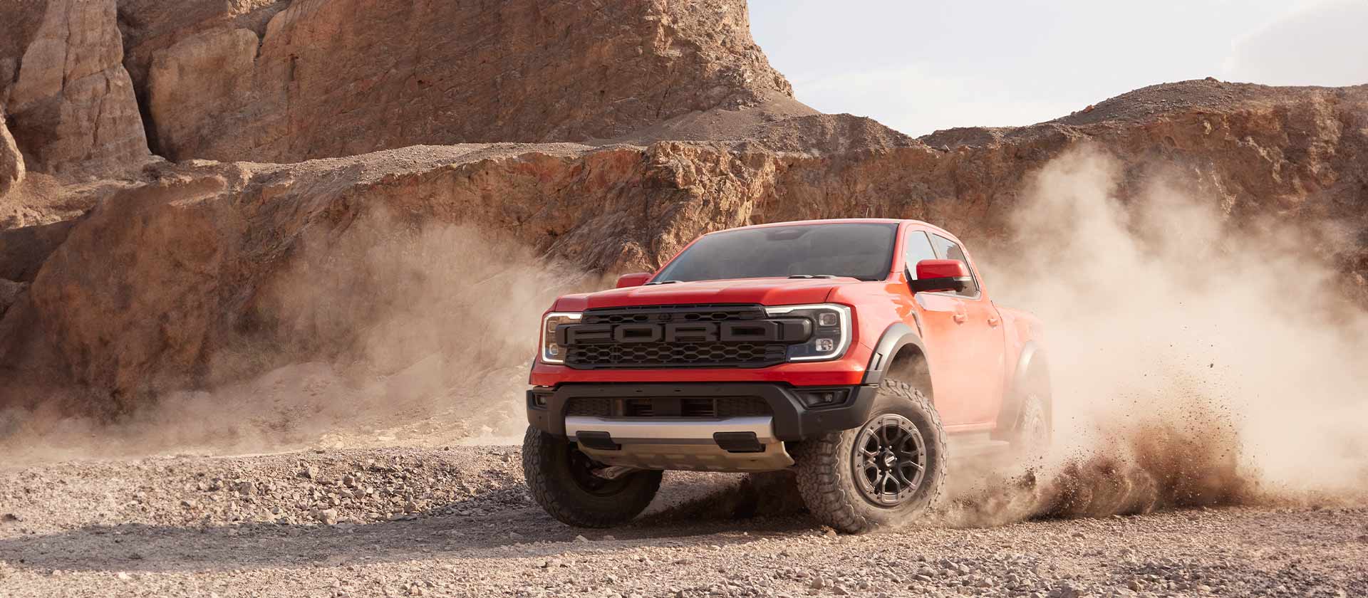 Code Orange Ford Ranger Raptor driving through crushed rock dust.