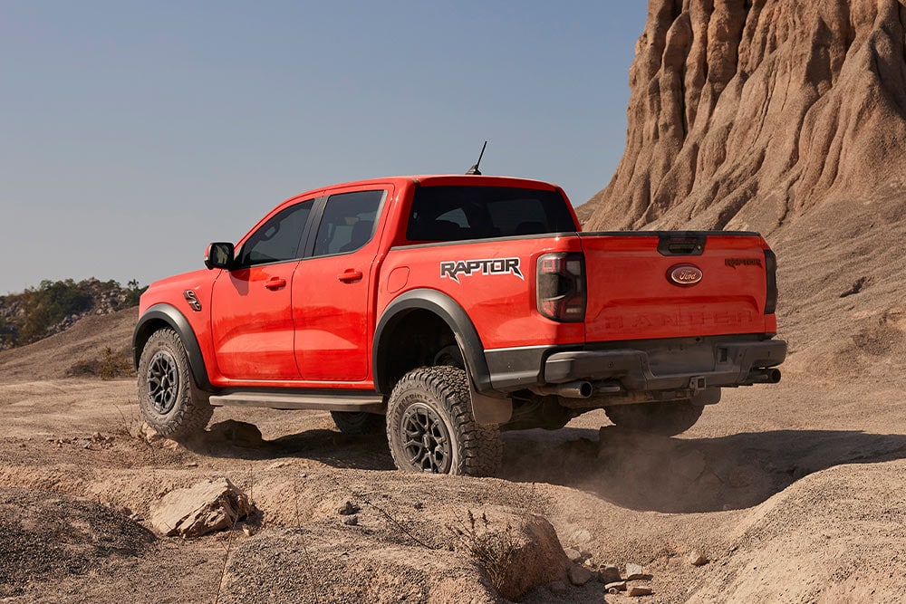 Code Orange Ford Ranger Raptor driving off-road uphill on rocks.