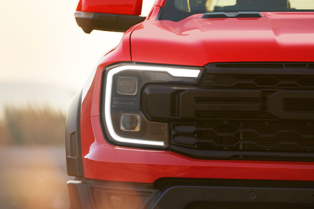 Close-up of a Code Orange Ford Ranger Raptor headlight and grill.