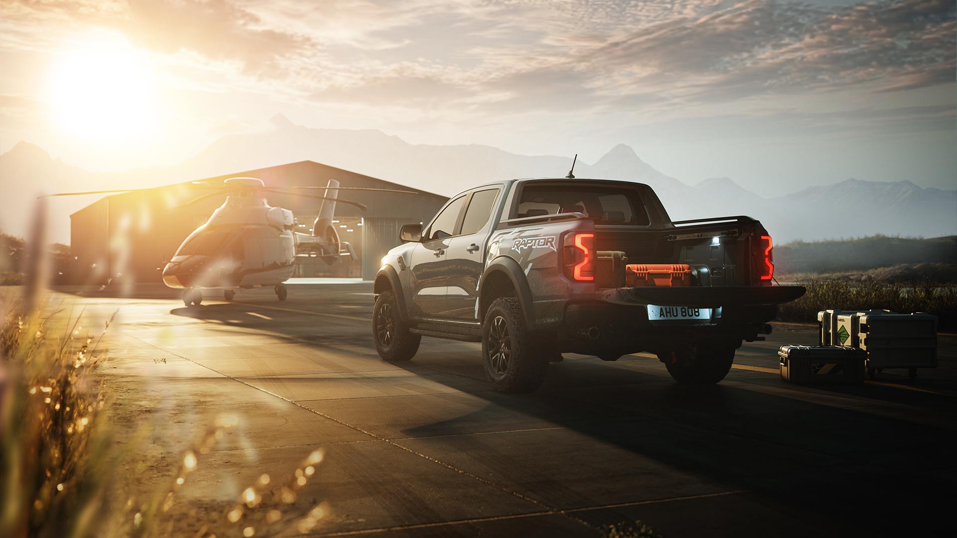 Ford Ranger Raptor parked next to a helicopter and plane hangar at sunset.