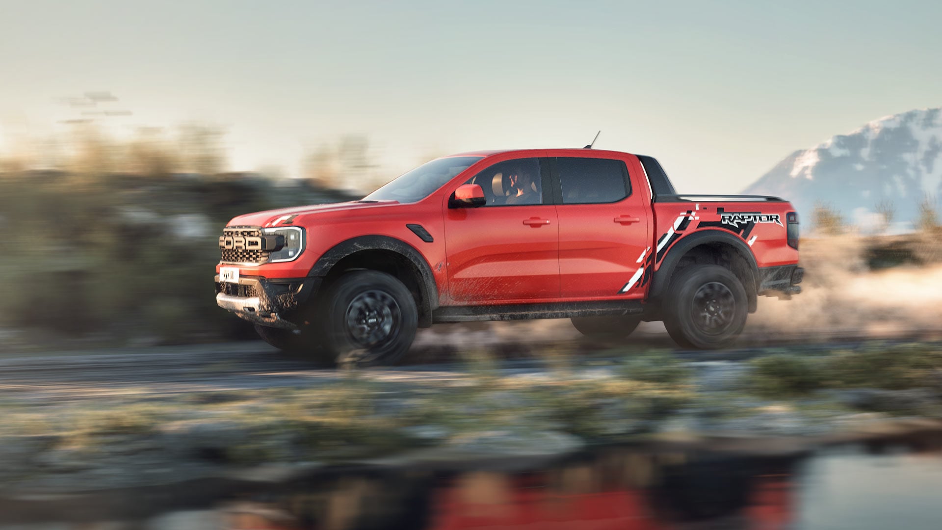 Red Ford Ranger Raptor driving through a mountainous landscape.