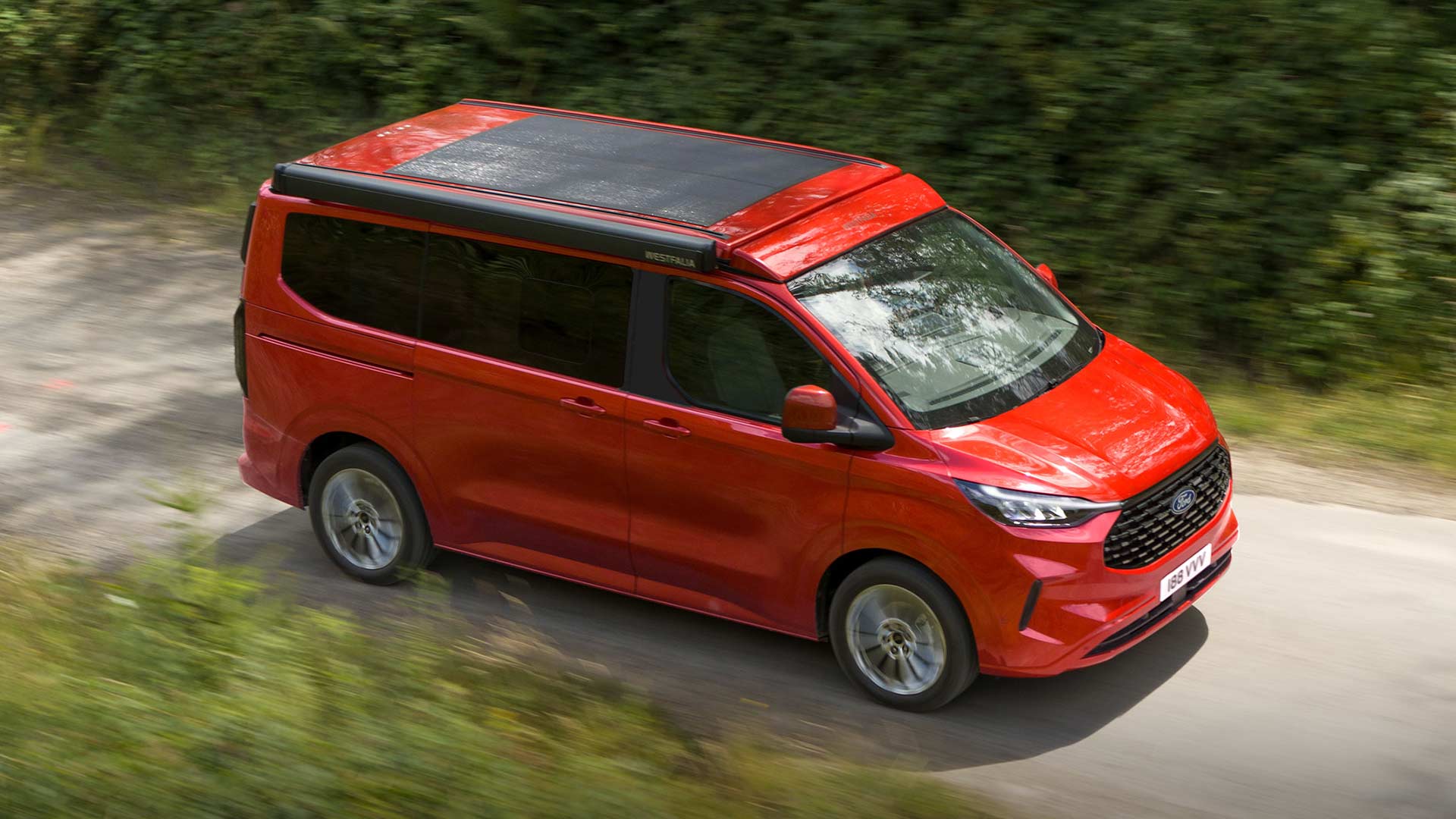 Red Ford Transit Custom Nugget driving on a dirt road.