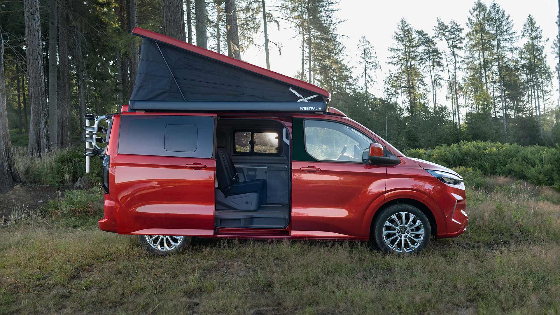 Red Ford Transit Custom Nugget is parked with self-folding fabric tilt roof up and sliding side door opened. 