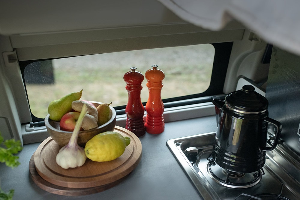 Ford Transit Custom Nugget integrated kitchen hob with kettle and fruit on the counter.
