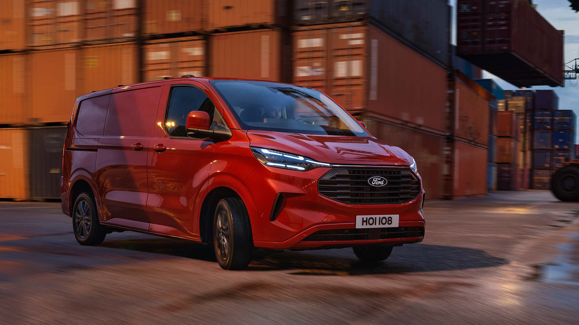 Red Ford Transit Custom van drives through a dock yard. 