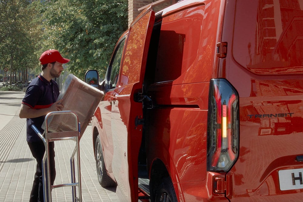 Delivery driver loading packages into a red Ford Transit Custom.