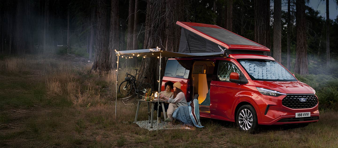 Red Ford Transit Custom Nugget camper van parked in a forest.