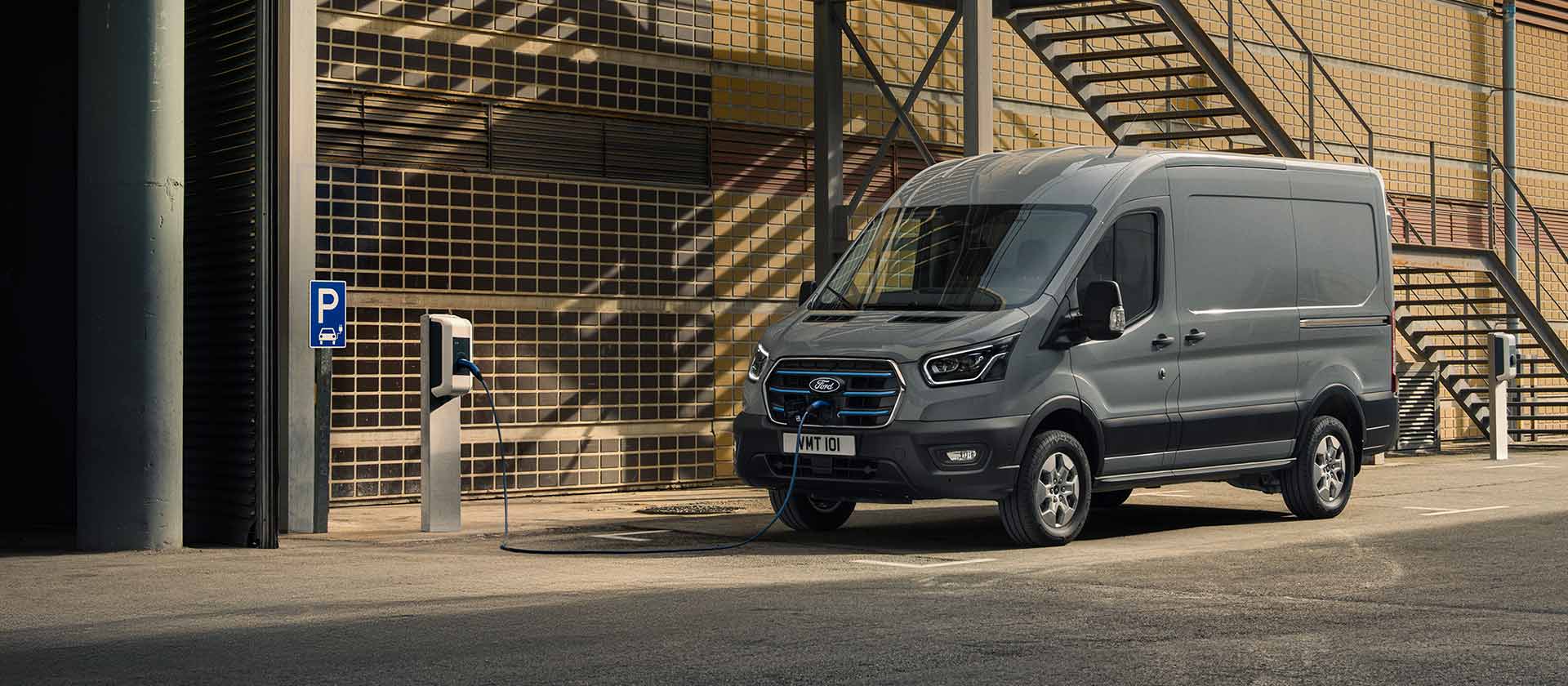 Gray Ford E-Transit electric van parked near a charging station.