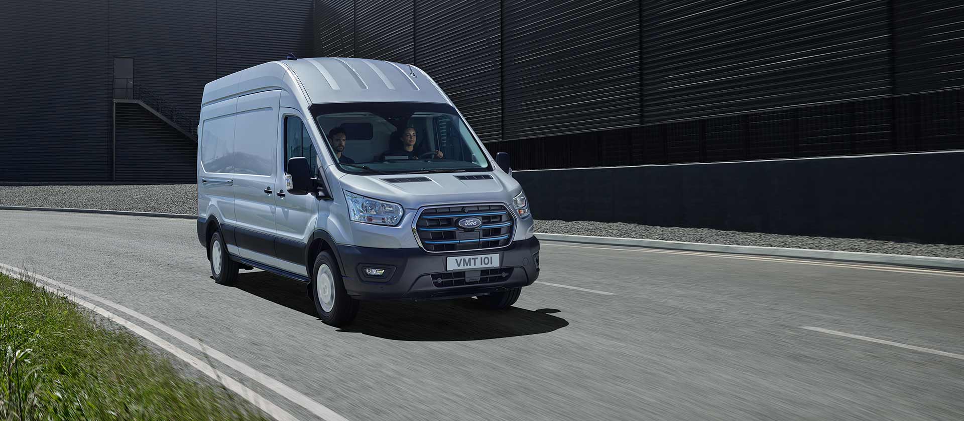 Silver Ford E-Transit electric van driving on a road.