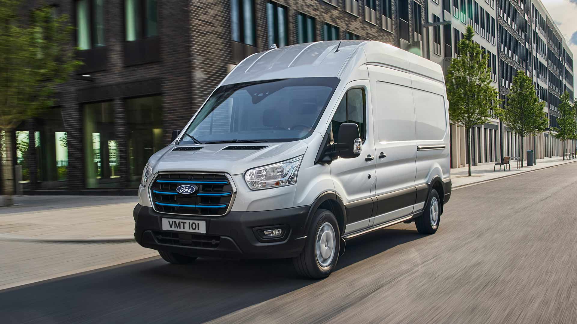 Silver Ford E-Transit electric van driving on a city street.