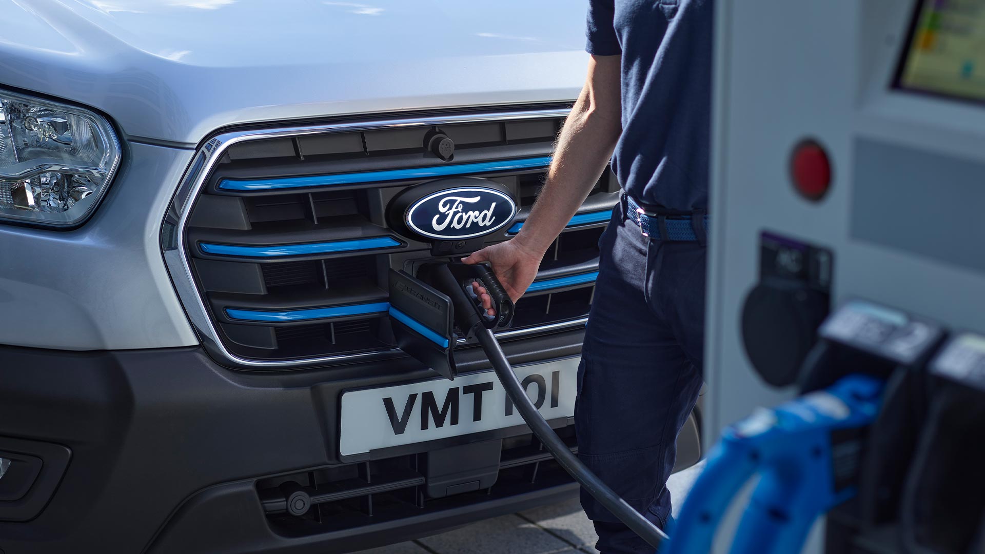 Close-up of a person plugging a charging cable into a silver Ford E-Transit electric van.