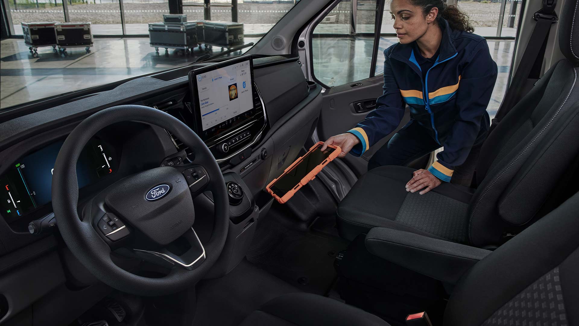 The interior of a Ford Transit van, showing a woman placing a tablet in a storage area.