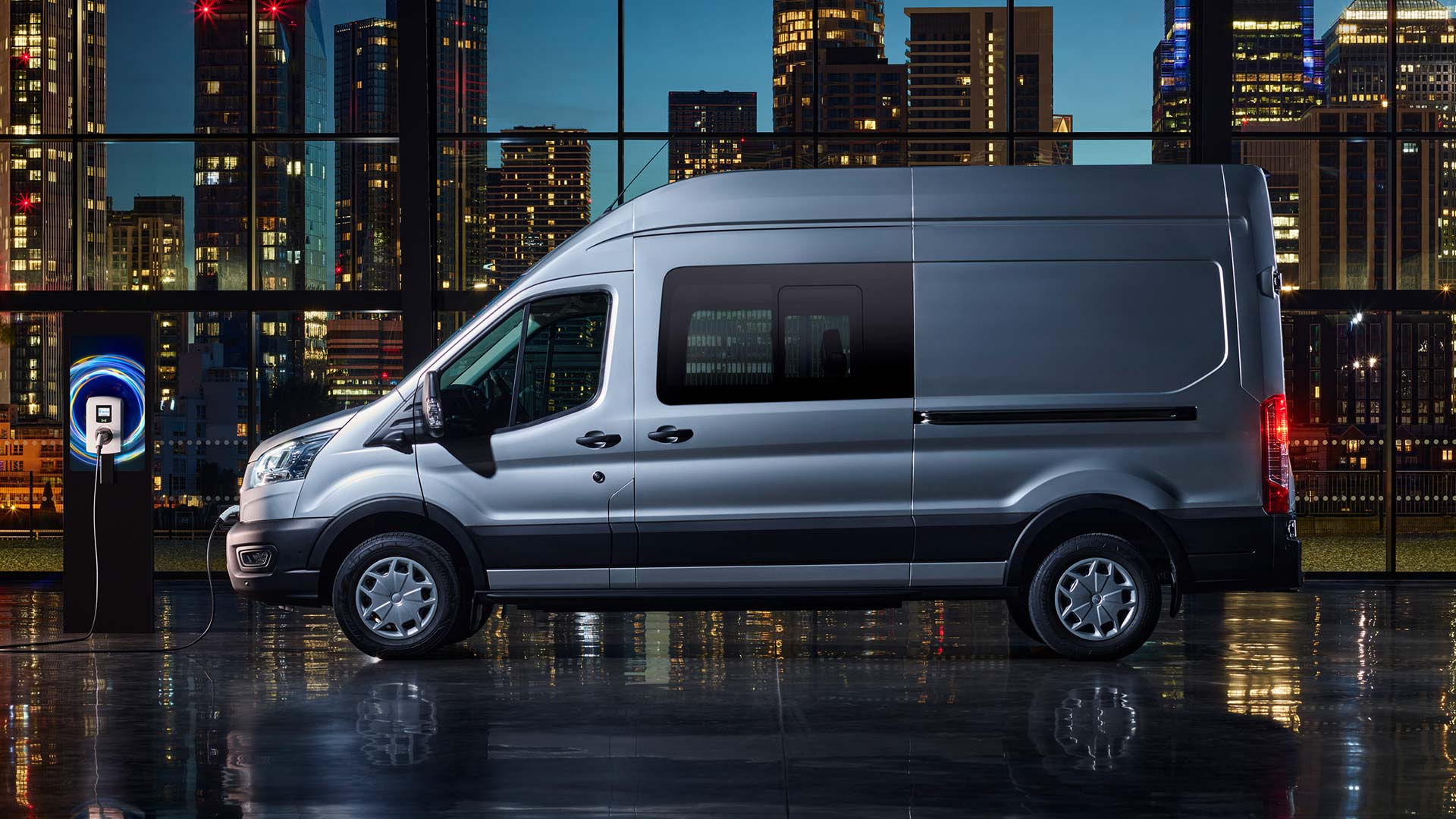Silver Ford E-Transit Double Cab-in-Van charging with a city skyline background.