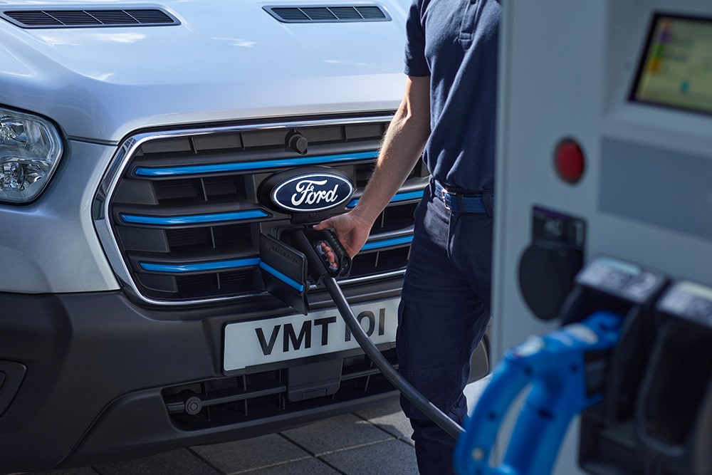 Close-up of a person plugging a charging cable into a silver Ford E-Transit electric van.