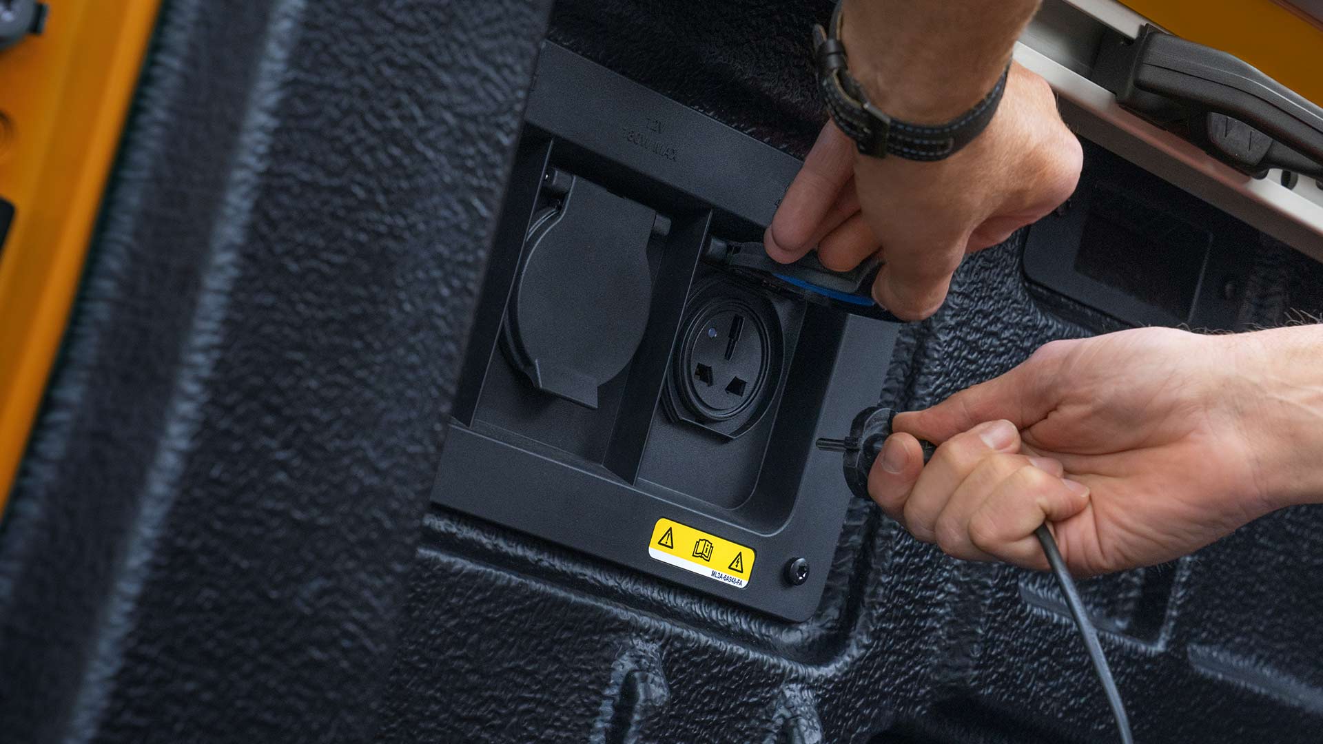 Close-up of hands connecting cables to the power outlet in thetruck bed of the Ford Ranger.