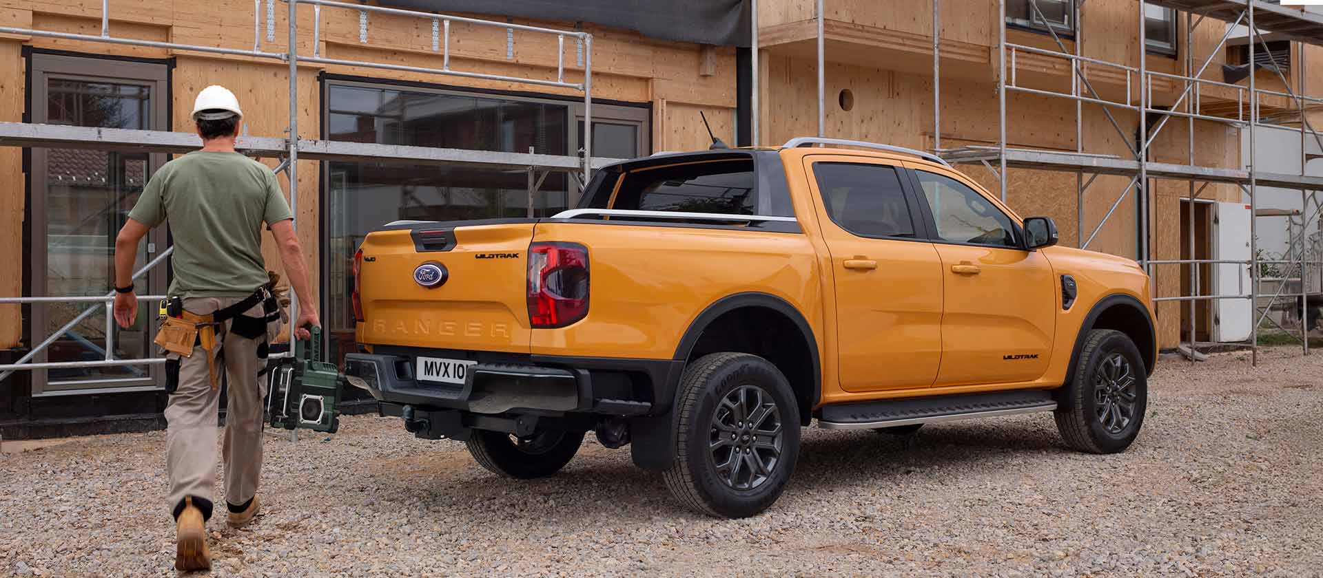 A worker in a hard hat walks towards a yellow Ford Ranger pick-up truck at a construction site.