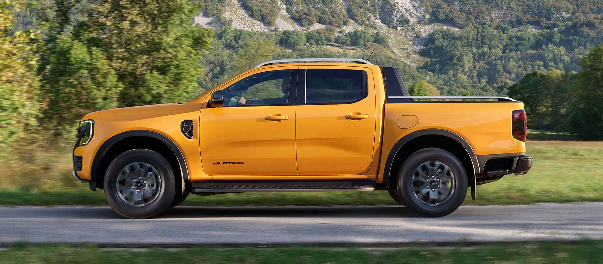 Side view of a yellow Ford Ranger Wildtrak driving on a paved road.