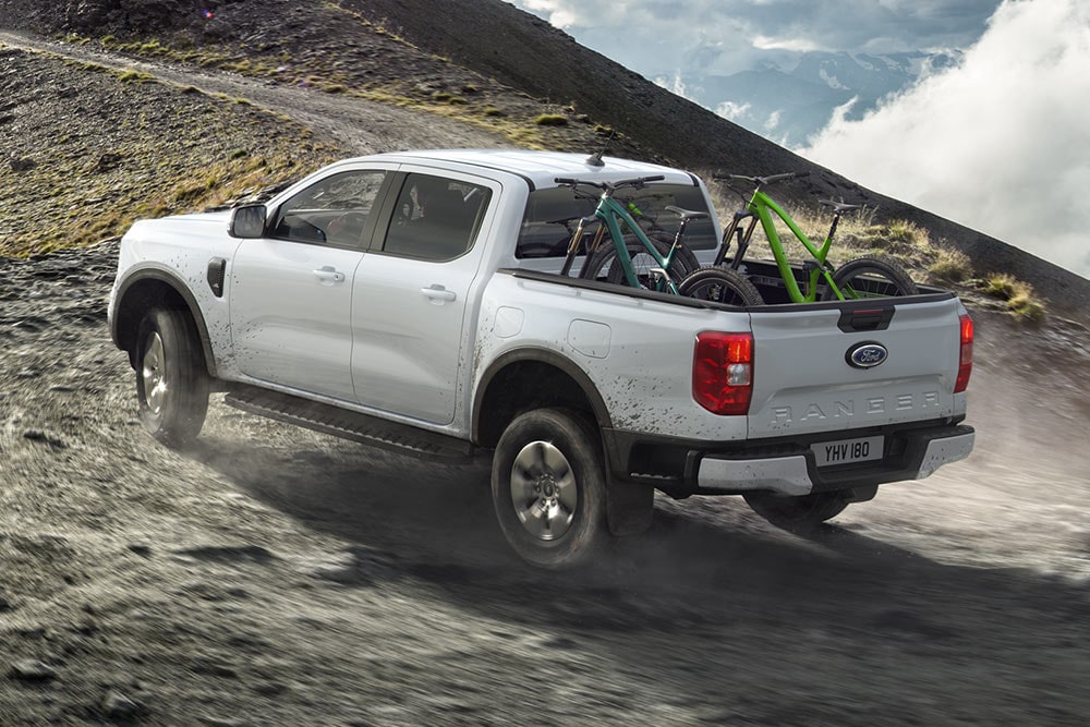 A Ford Ranger Stormtrak PHEV drives off road up a hill with two bikes in the loadspace.