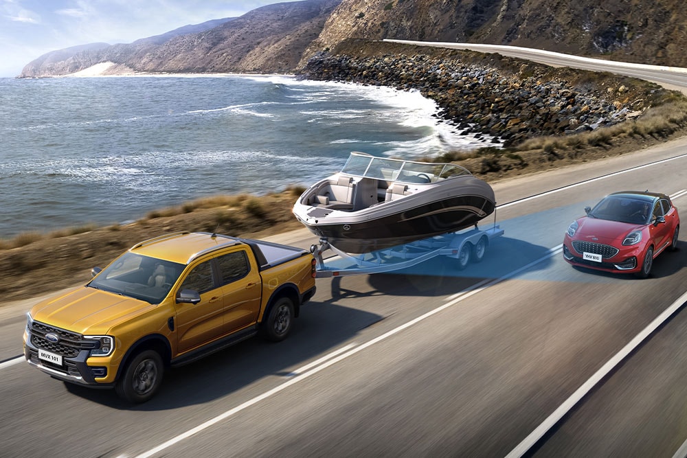  A yellow Ford Ranger tows a boat along a coastal highway, demonstrating its towing capacity.