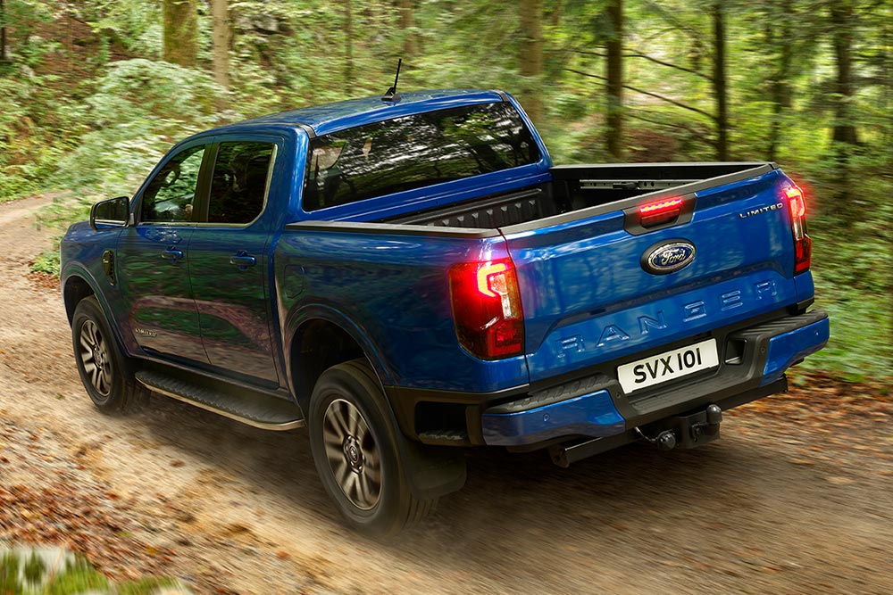  Rear taillight and tailgate view of a blue Ford Ranger pick-up truck driving on a dirt road.
