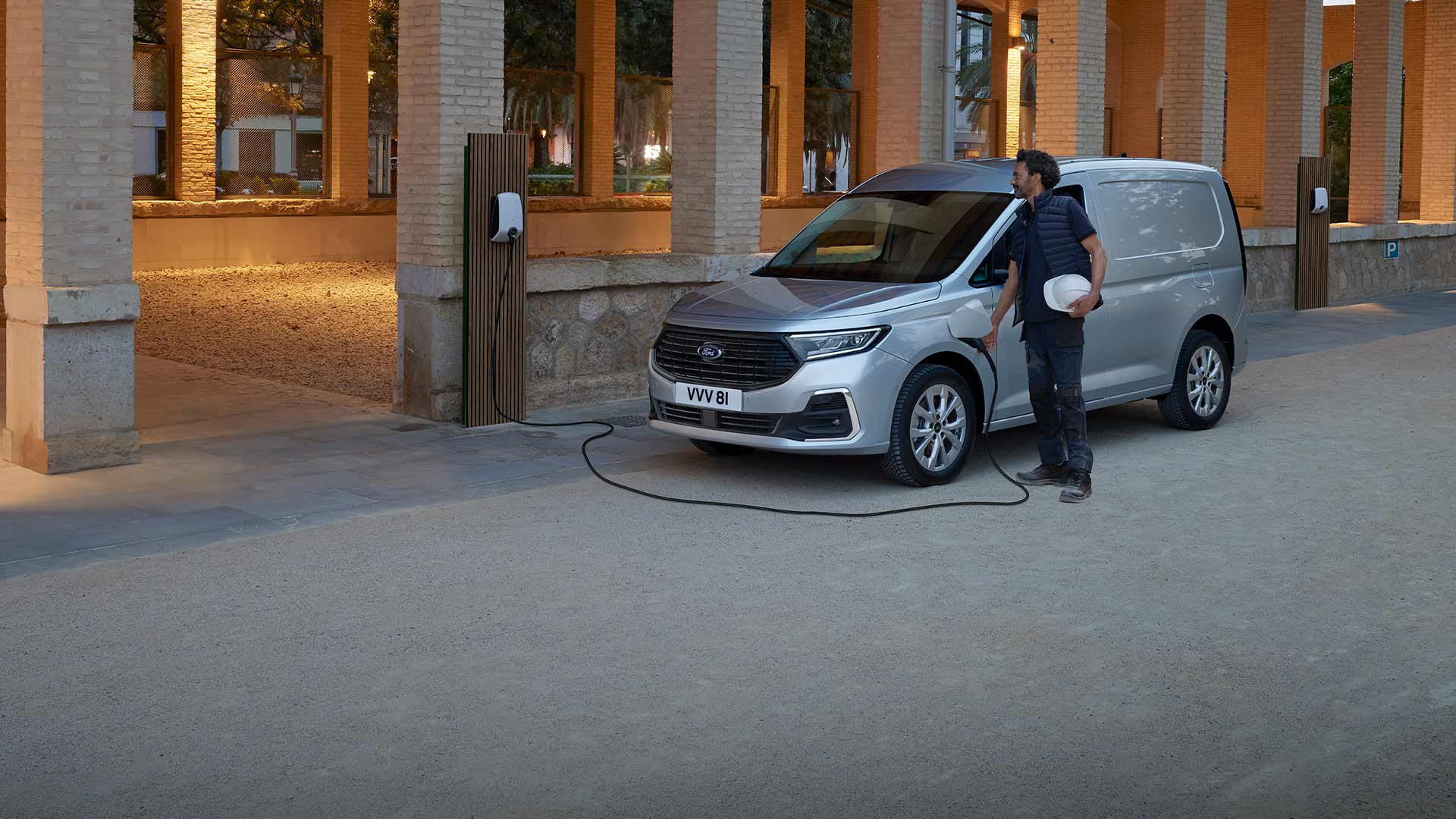 A man charges a Ford Transit Connect plug-in hybrid van at an outdoor charging point.
