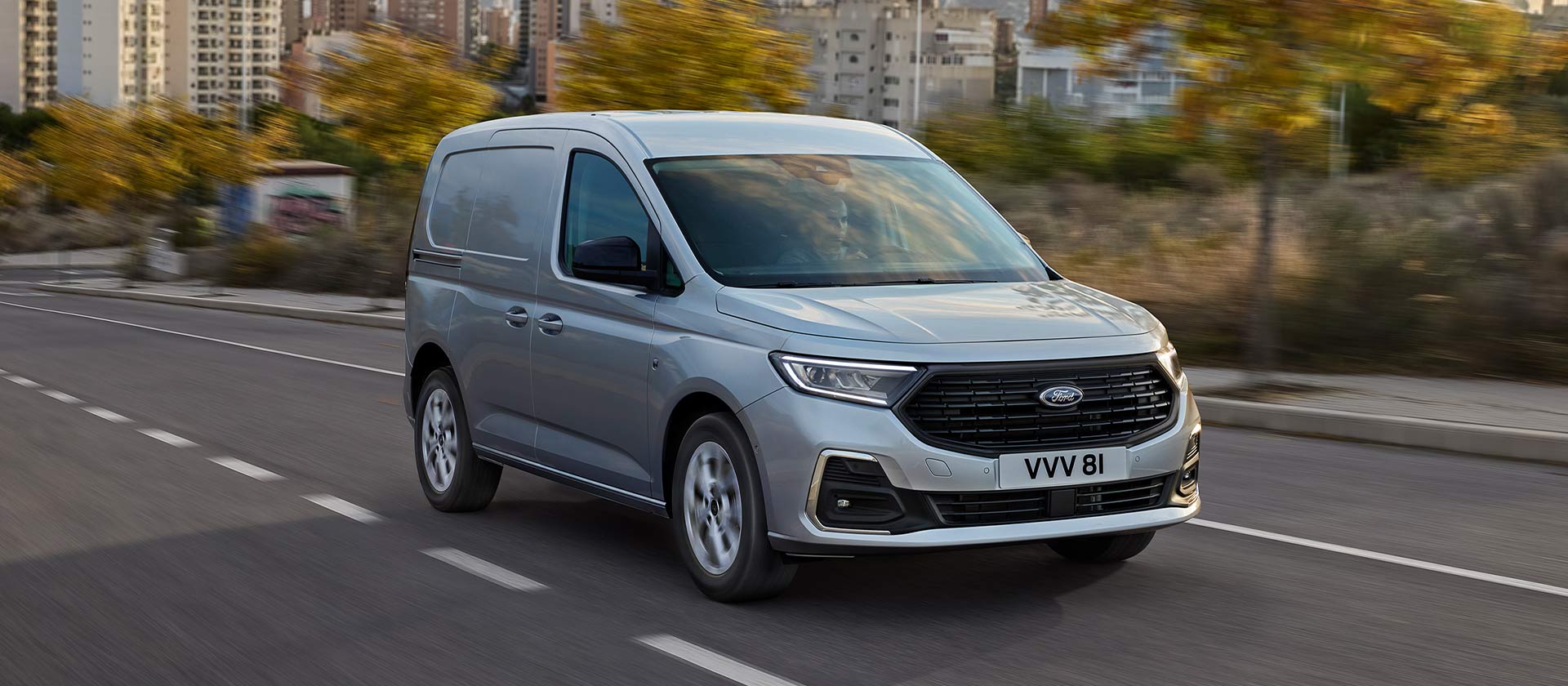 Ford Transit Connect driving in a city, showing chrome exterior fog lamp surrounds and automatic headlights.