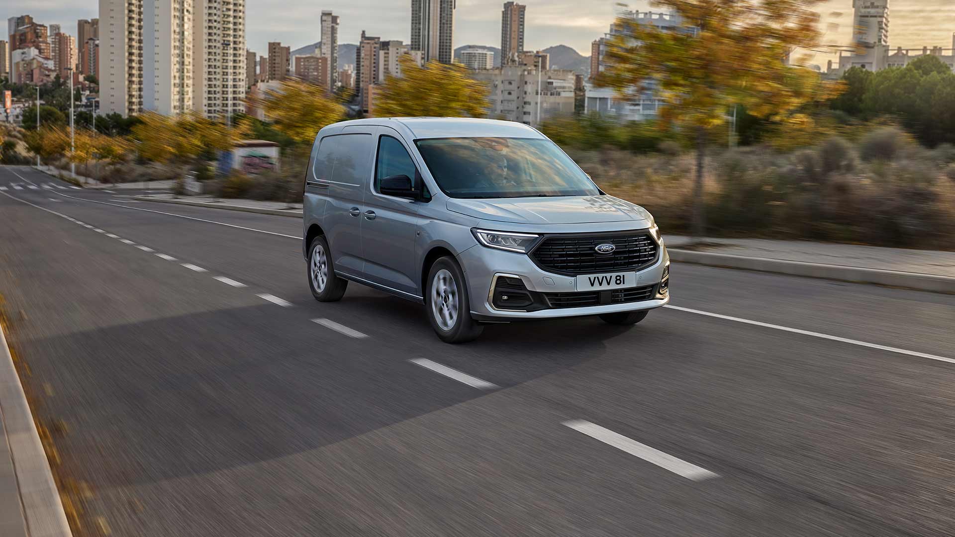 Ford Transit Connect driving in a city, showing chrome exterior fog lamp surrounds and automatic headlights.