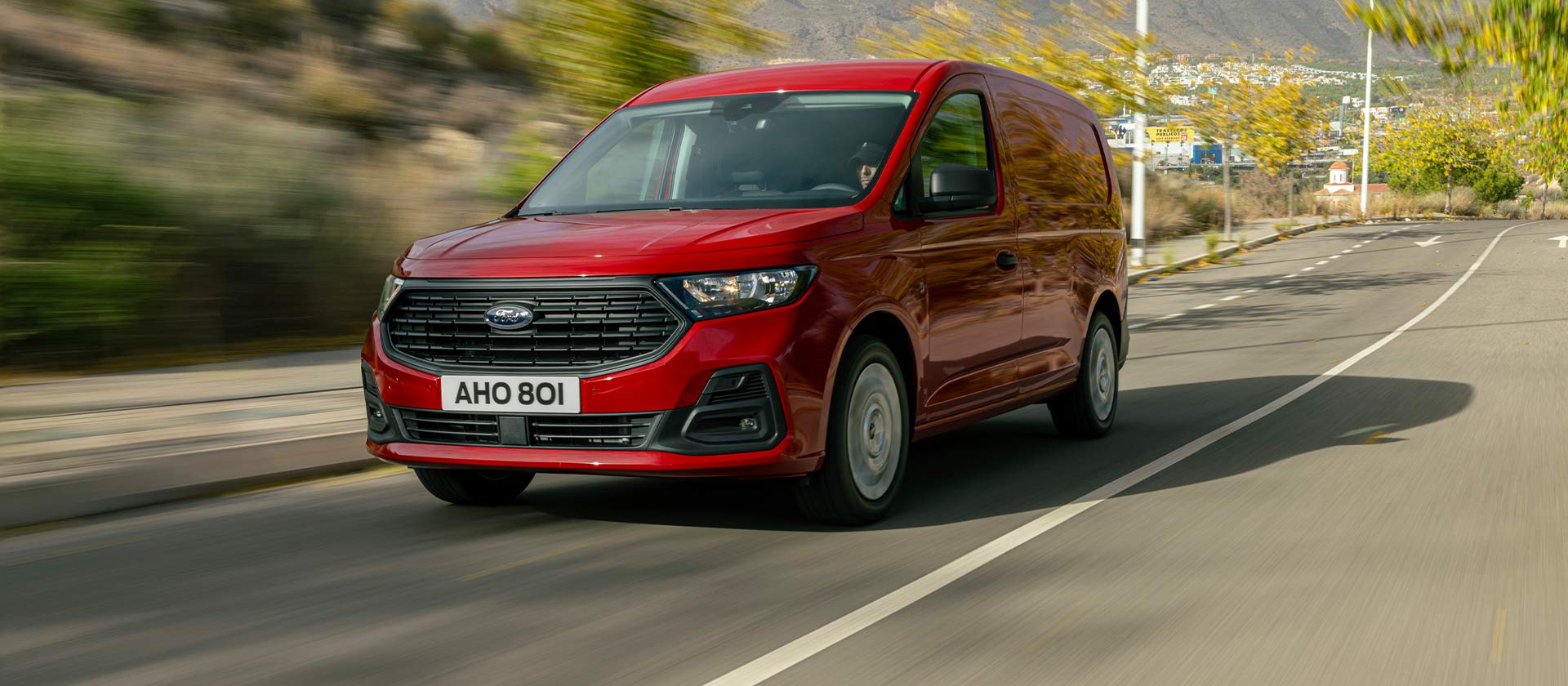 Ford Transit Connect driving on a road, showing the front grille and automatic headlights.