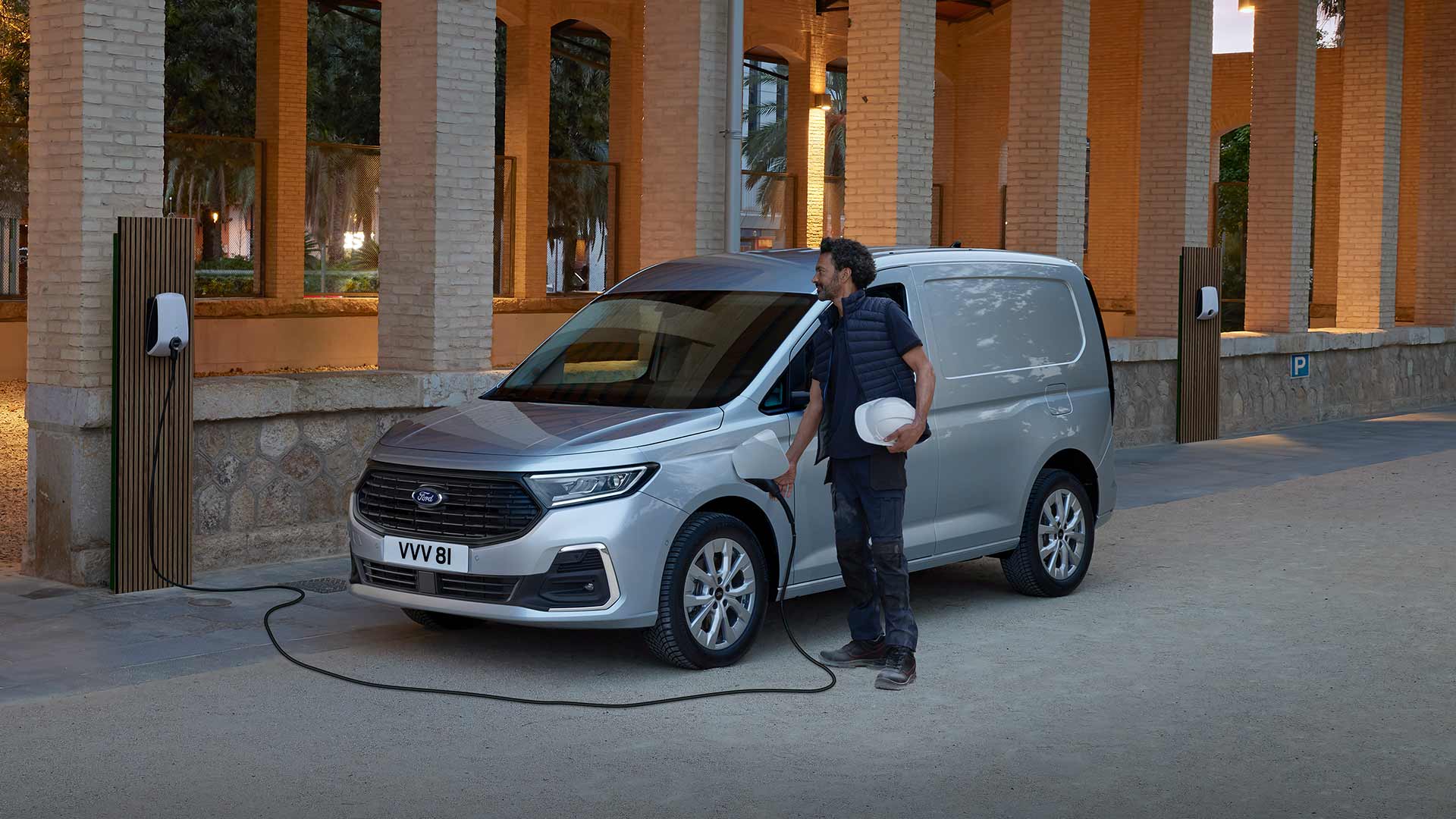 A man charges a Ford Transit Connect plug-in hybrid van at an outdoor charging point.