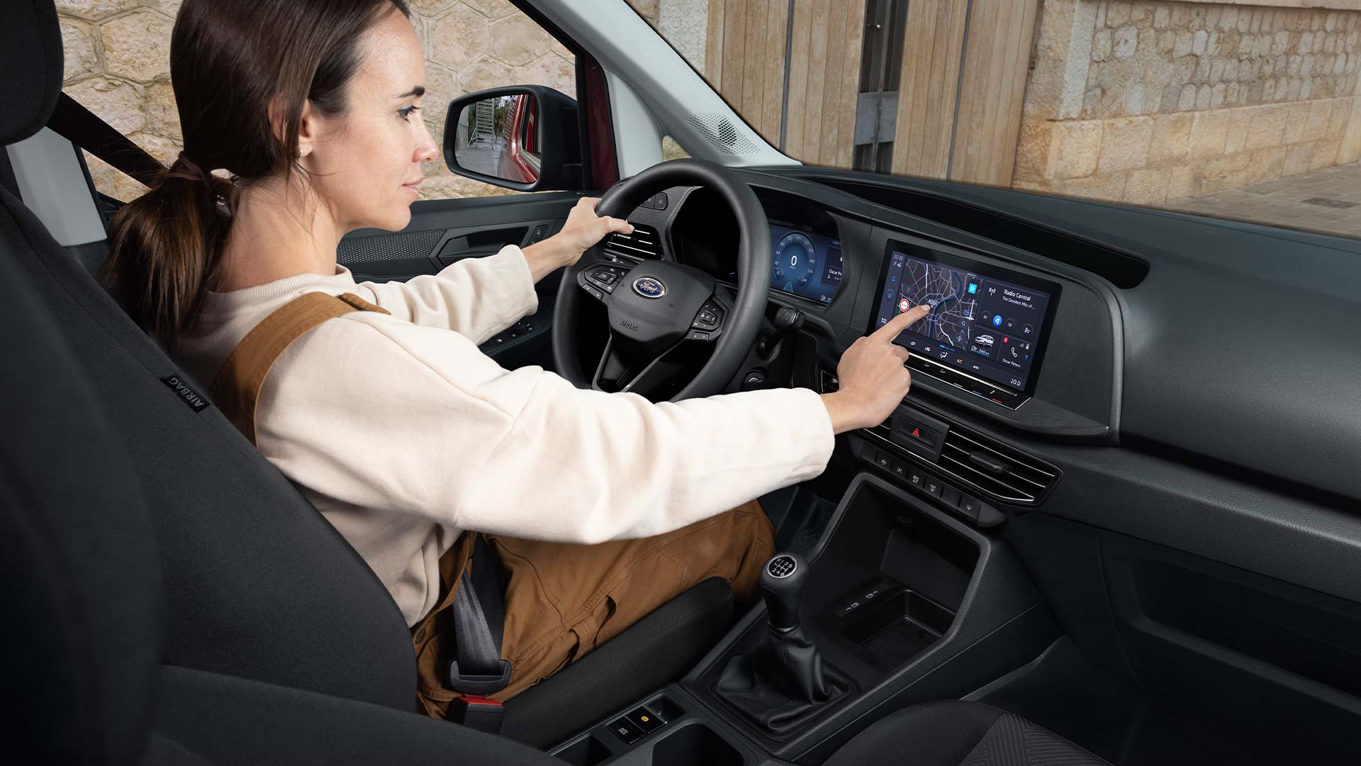 A woman sits in the driving seat of a Ford Transit Connect, using the 10-inch colour touchscreen.