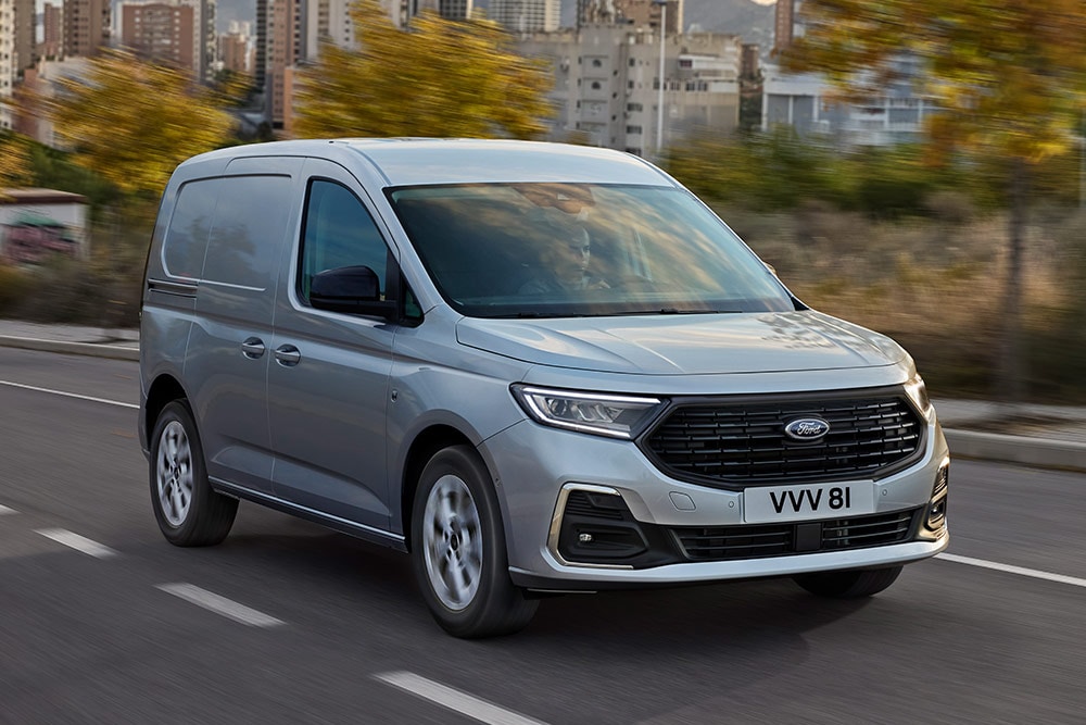 Ford Transit Connect driving in a city, showing chrome exterior fog lamp surrounds and automatic headlights.