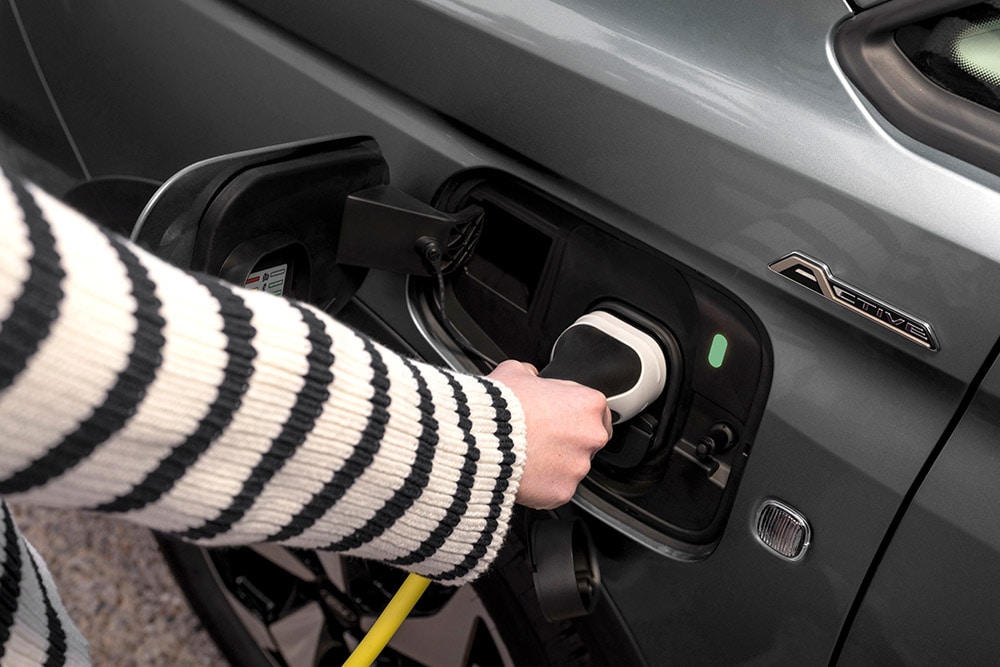 A person plugging a charging cable into a Ford Transit Connect plug-in hybrid.