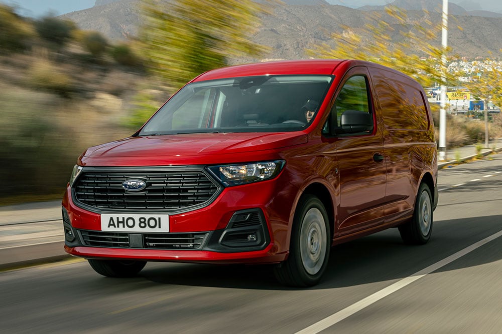 Ford Transit Connect driving on a road, showing the front grille and automatic headlights.
