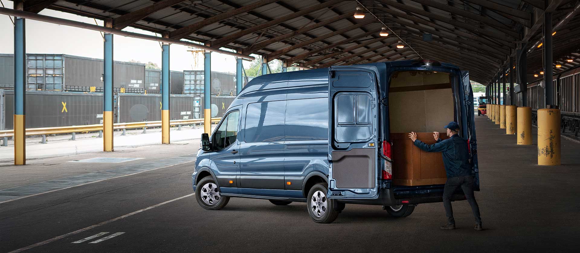 A man loads cargo into the open doors of a Ford Transit Van.