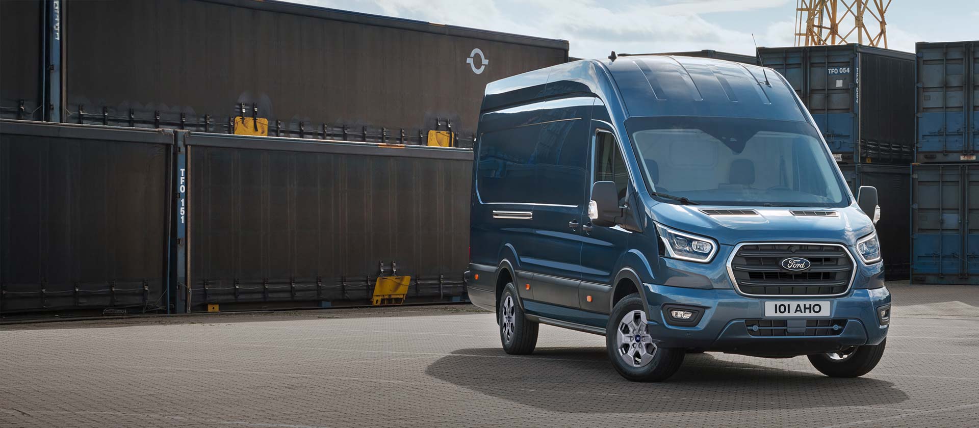 Blue Ford Transit Van parked in front of shipping containers.