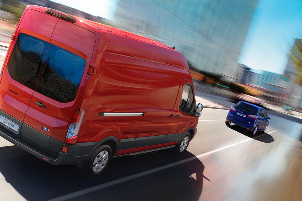 Red Ford Transit van driving on a road.