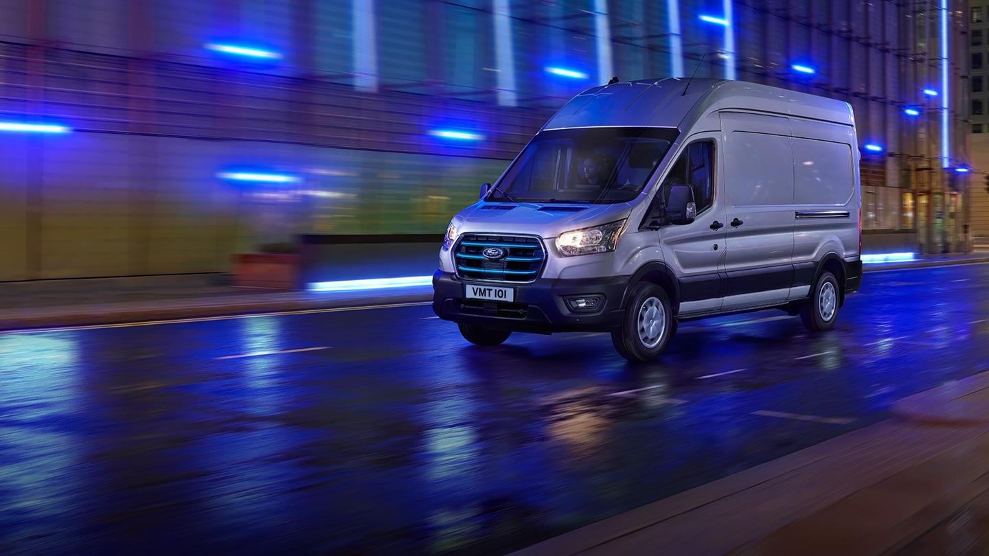 Ford E-Transit Van with headlights on driving along street at night.