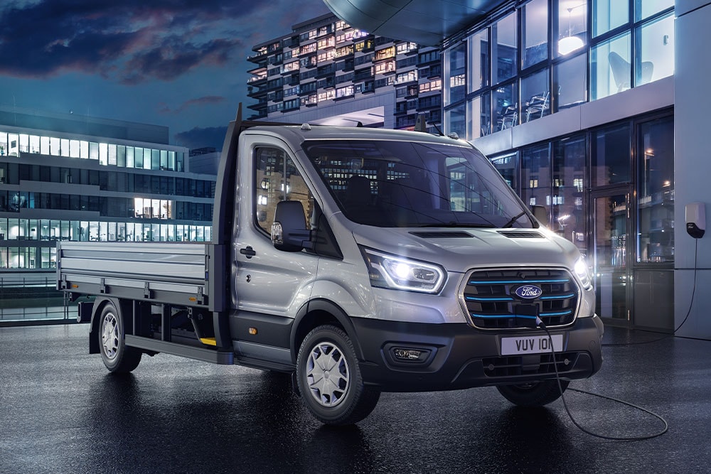 Silver Ford Transit chassis cab parked in front of a modern building at night.