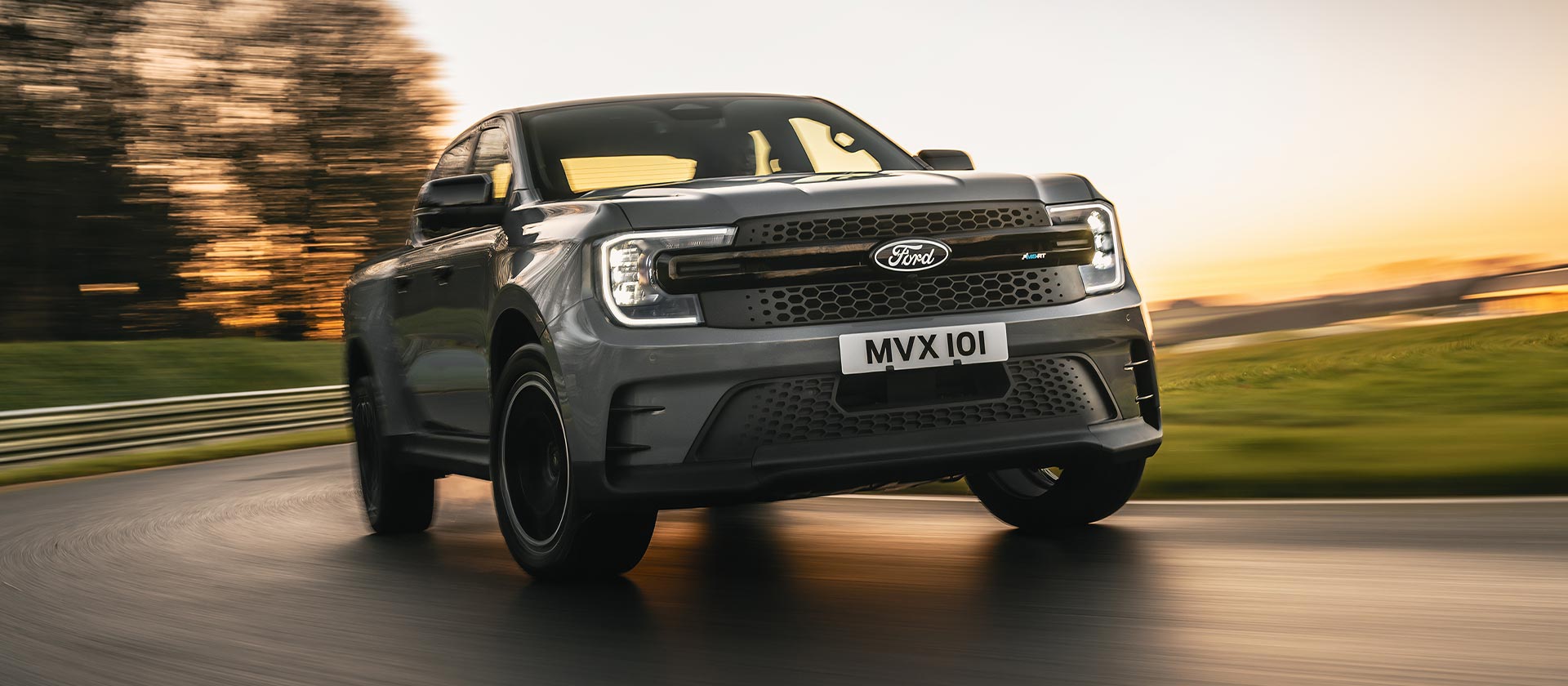Honeycomb grille and headlight view of a Ford Ranger MS-RT driving along a track at sunset.