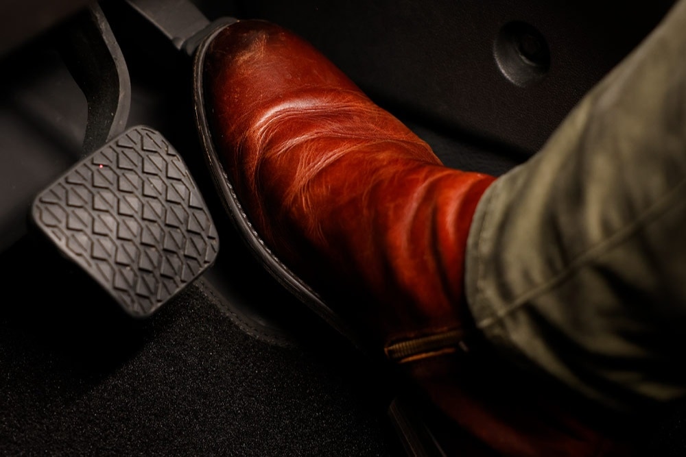 A person's foot in a brown boot resting on the accelerator pedal of a vehicle.