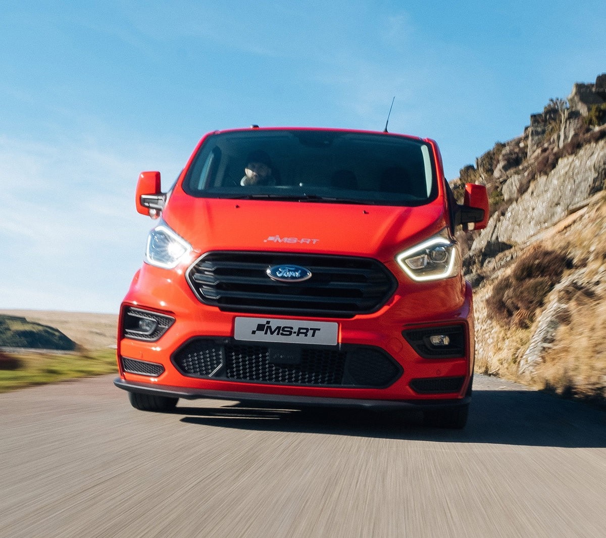 Red Ford Transit Custom MS-RT driving next to a mountain side 