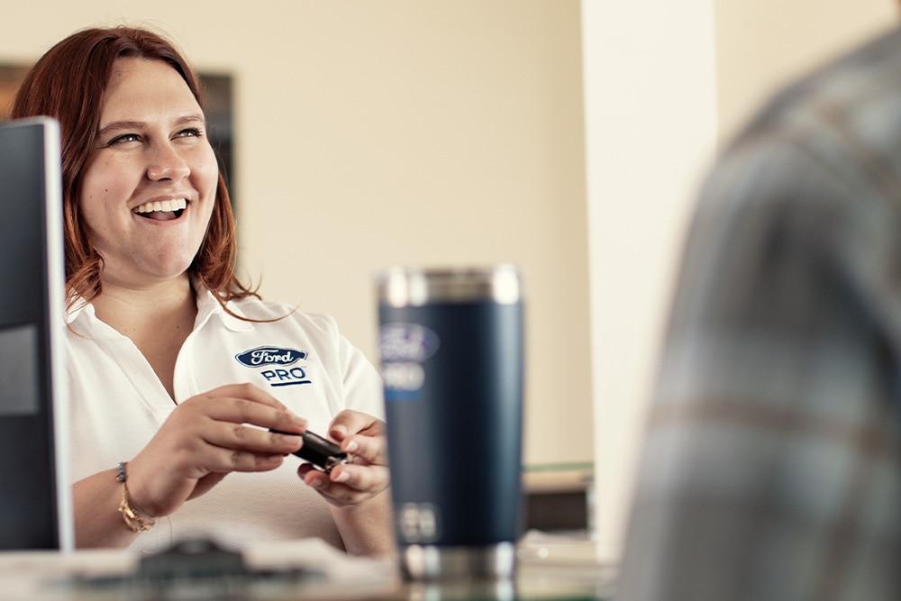 A Ford manager at her desk, smiling while talking with a customer.